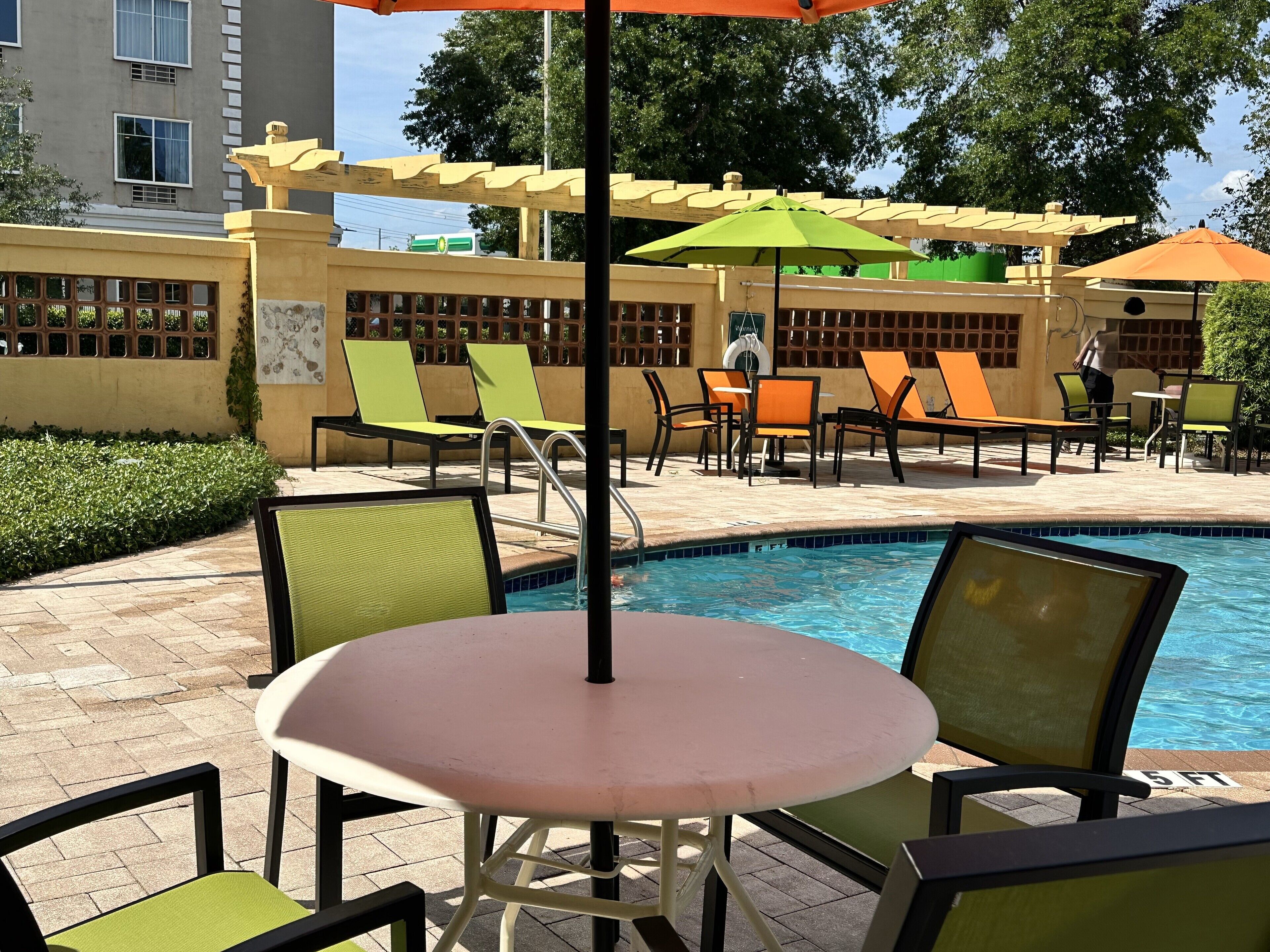 A poolside area with lounge chairs, a table, and umbrellas.