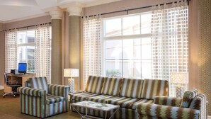 Sala de estar con sofá, sillón y mesa de centro, un escritorio con ordenador y ventanas grandes con cortinas.