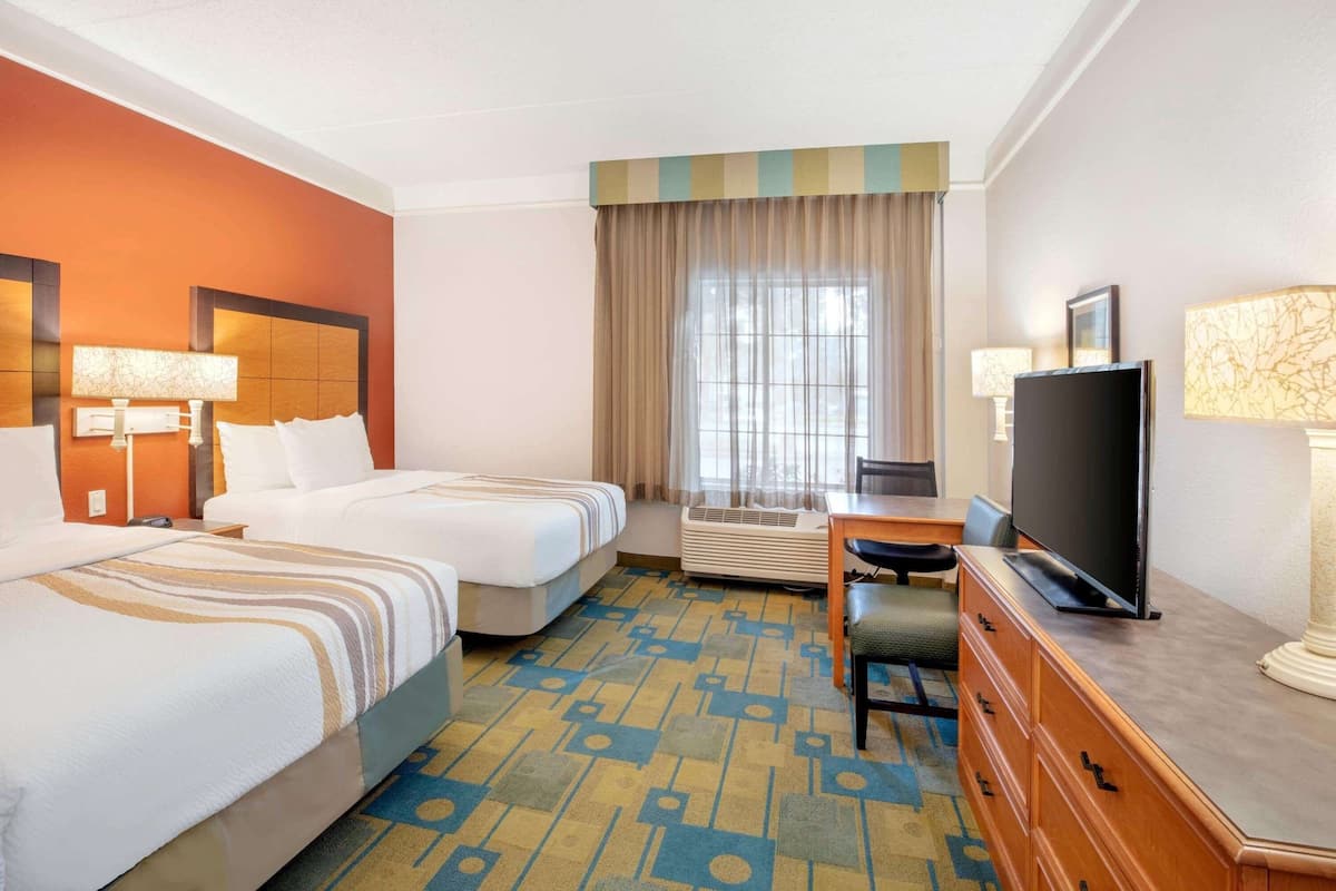 A hotel room with two beds, a desk, a television, and a window with curtains.