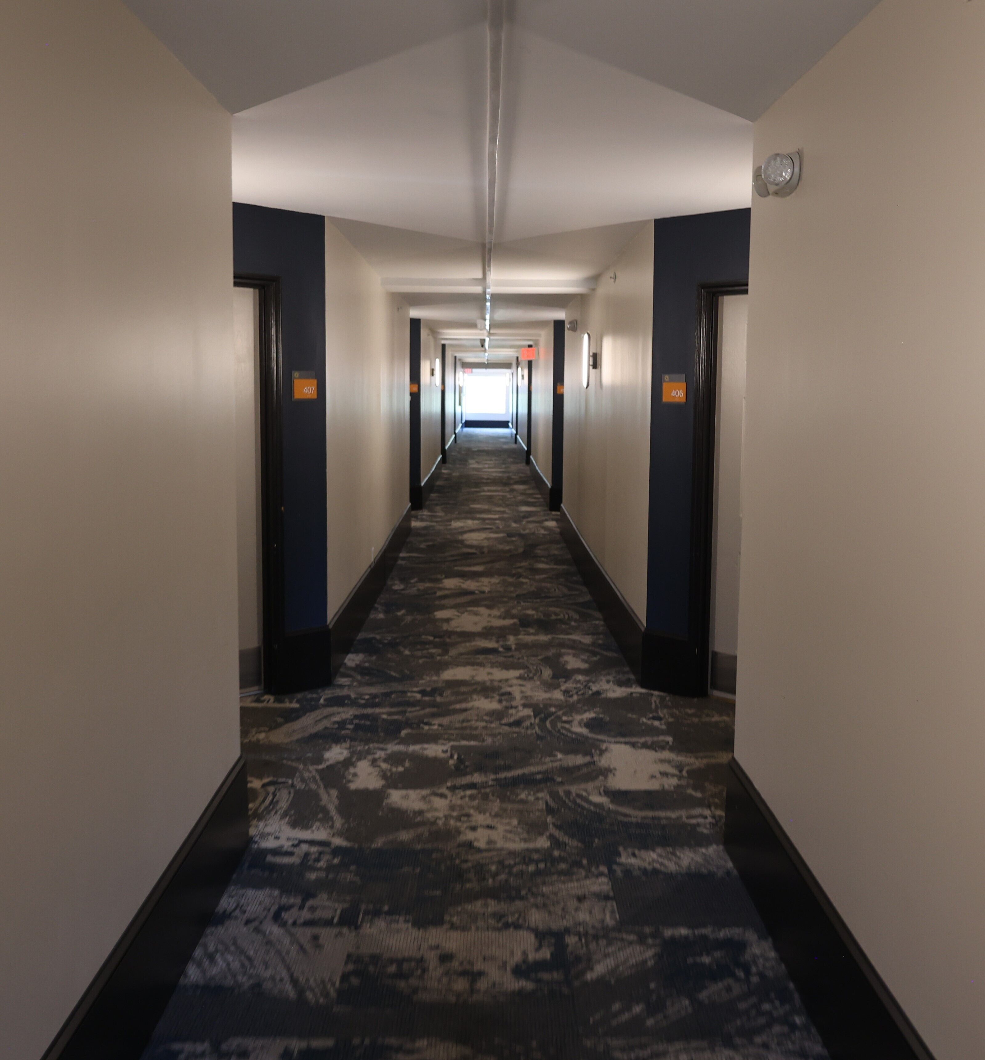 A hotel hallway with carpeted floors, dark walls, and doors numbered 407 and 406.