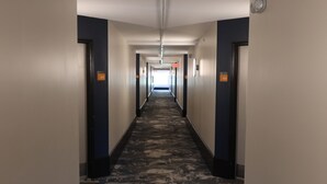 Un pasillo de hotel con pisos alfombrados, paredes oscuras y puertas con los números 407 y 406.