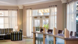 Un vestíbulo con mostrador de recepción, zona de estar y ventanas amplias con cortinas estampadas.