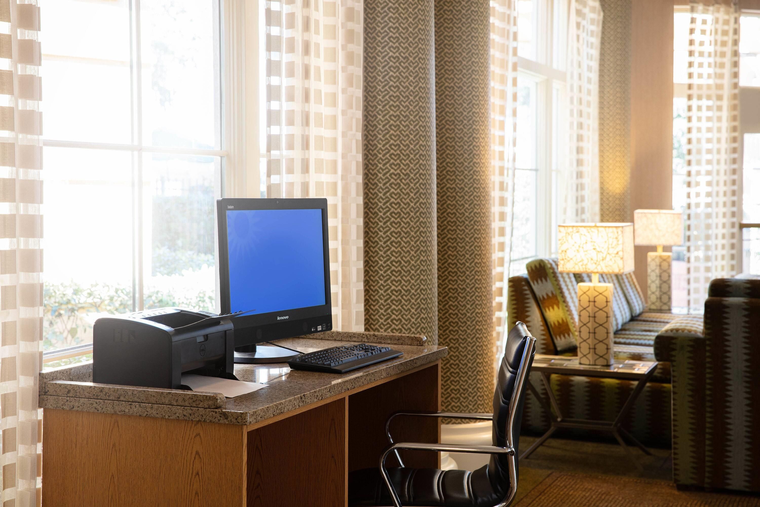 Une chambre d’hôtel équipée d’un bureau, d’un ordinateur, d’une imprimante et d’un coin salon avec un canapé et des fauteuils.