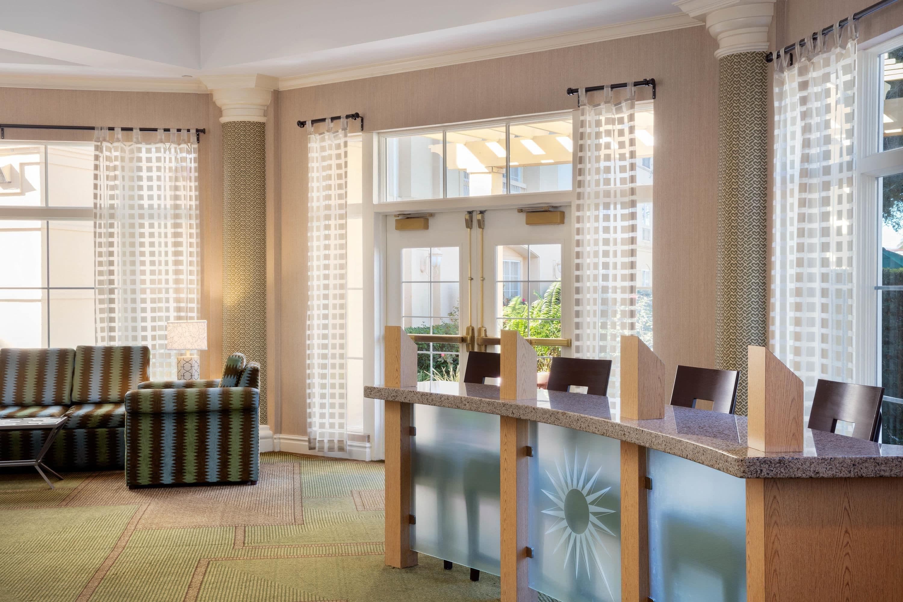 Eine Hotelhalle mit einer Rezeption, einer Sitzecke und großen Fenstern.