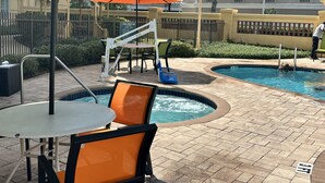 Un área de piscina con jacuzzi, sillones de descanso y una mesa.