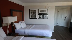 Habitación de hotel con dos camas, una mesita de noche, una lámpara y cuadros en la pared.