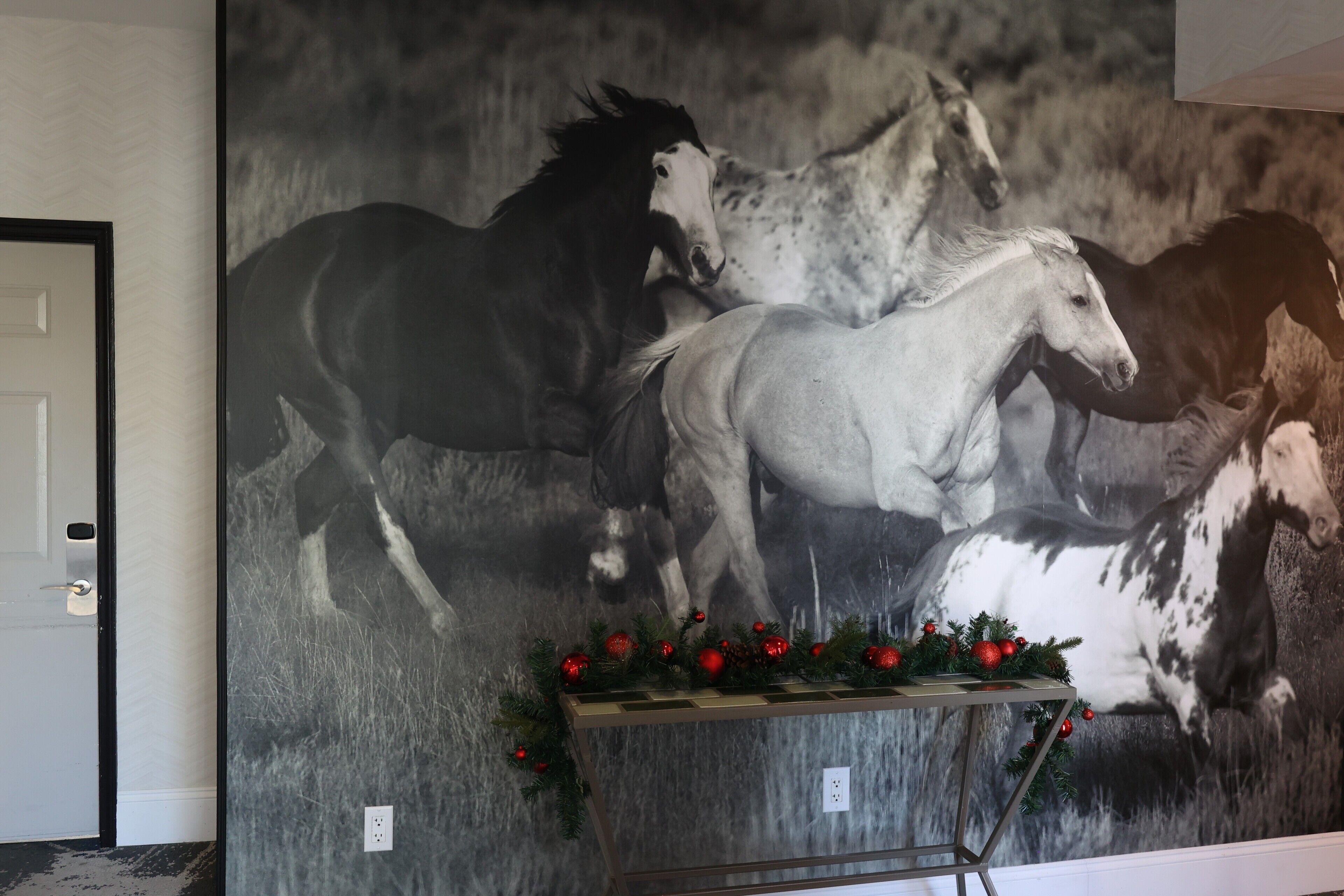 A large black and white horse mural on a wall with a small table decorated with red ornaments in front of it.