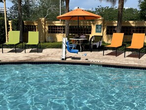 A pool area with clear water, lounge chairs, and a table with umbrellas.