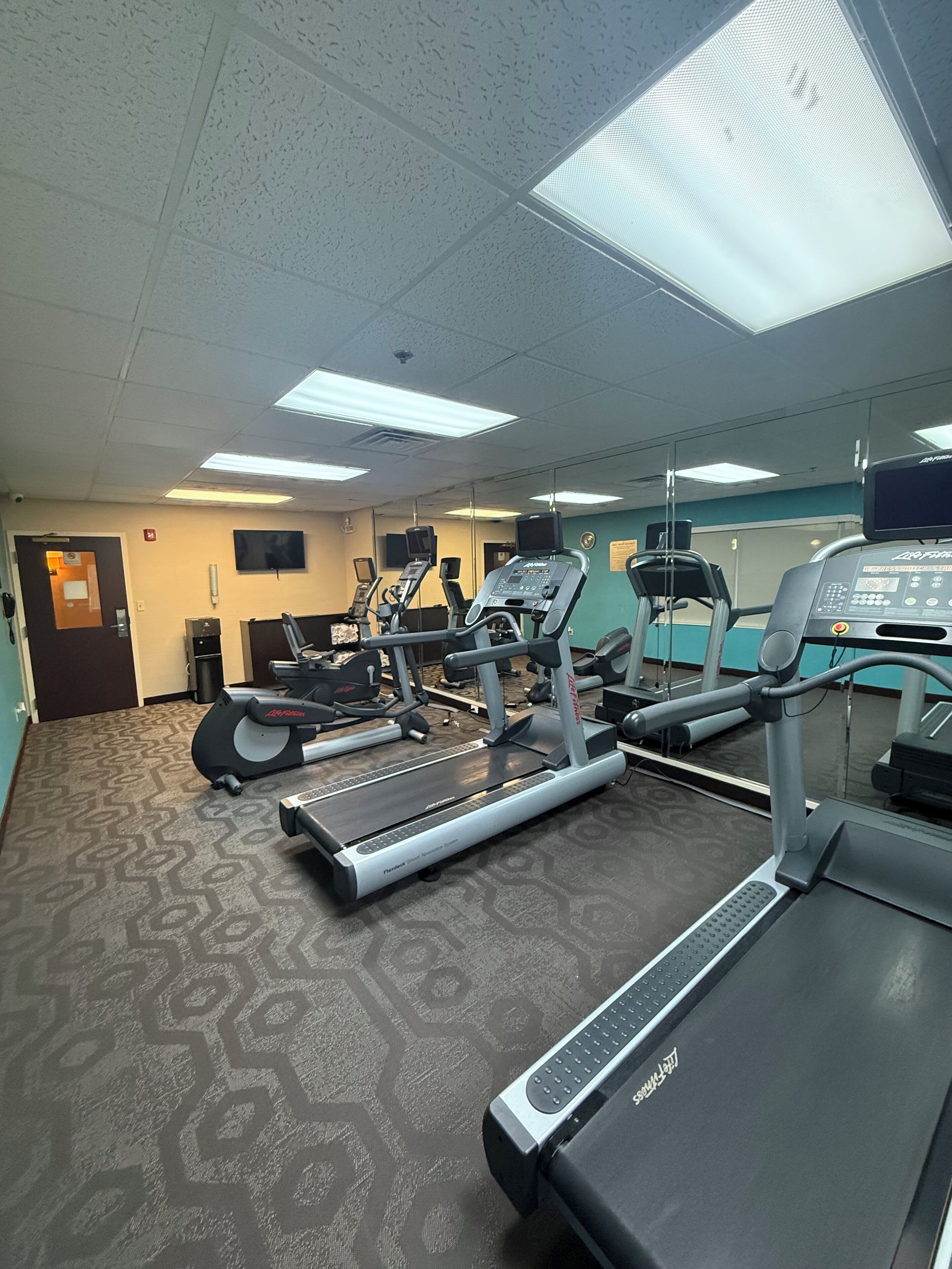Un gimnasio con cintas de correr, bicicletas estáticas y un espejo grande.