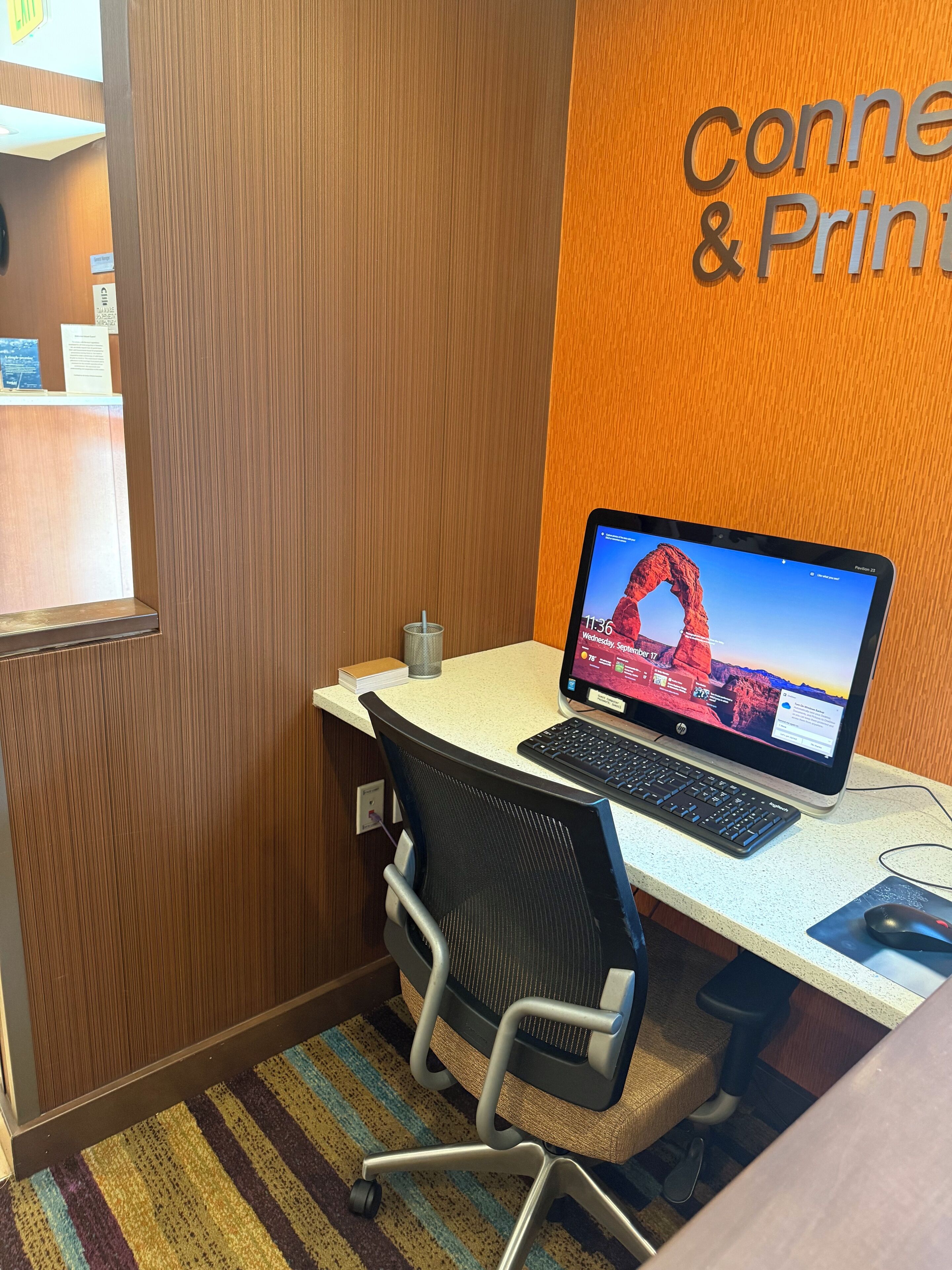 A workspace with a laptop, keyboard, and mouse on a desk, a chair, and a wall with a sign reading "Connect & Print".