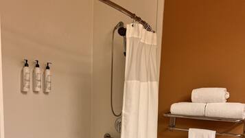 Un espace douche avec un rideau blanc, une porte de douche en verre et un porte-serviettes avec des serviettes.