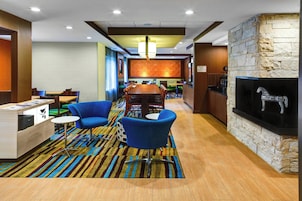 Un hall de hotel con un mostrador de recepción de madera, sillas azules, alfombra a rayas, chimenea de piedra y una zona de bar al fondo.