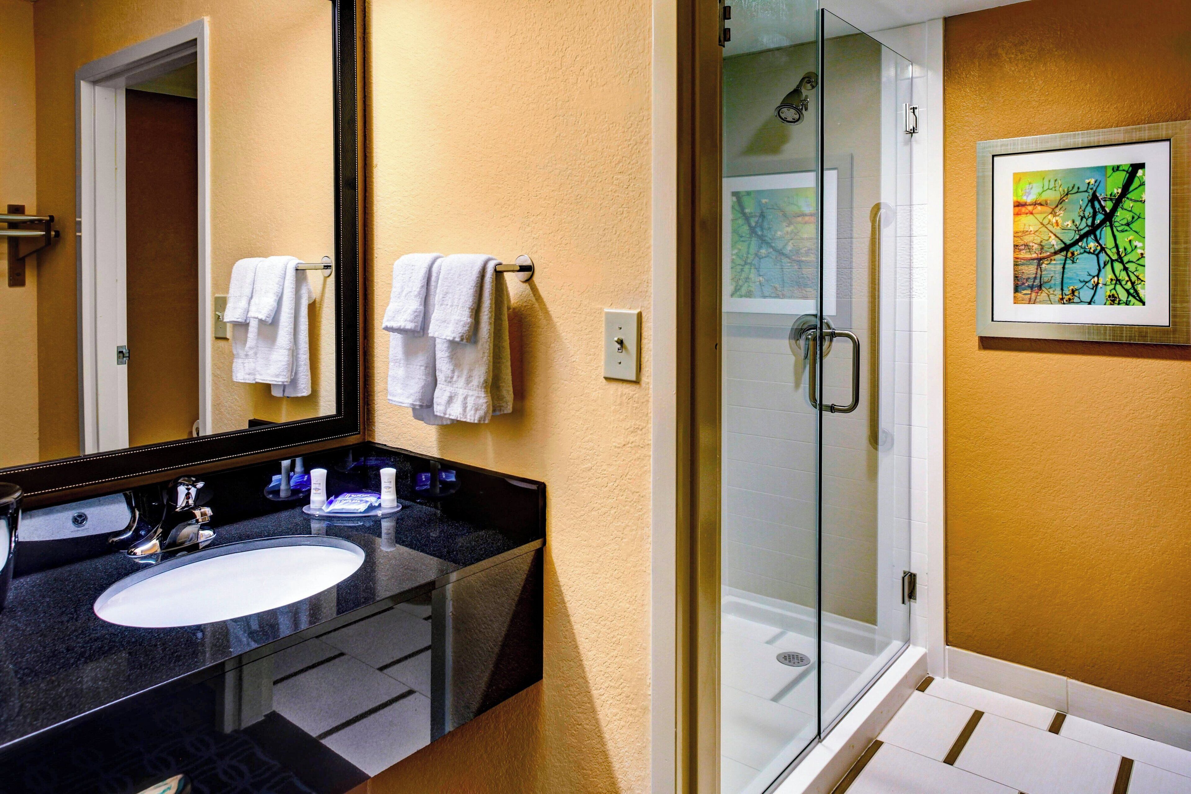 A bathroom with a black countertop sink, white towels, a glass shower enclosure, and a framed artwork on the wall.