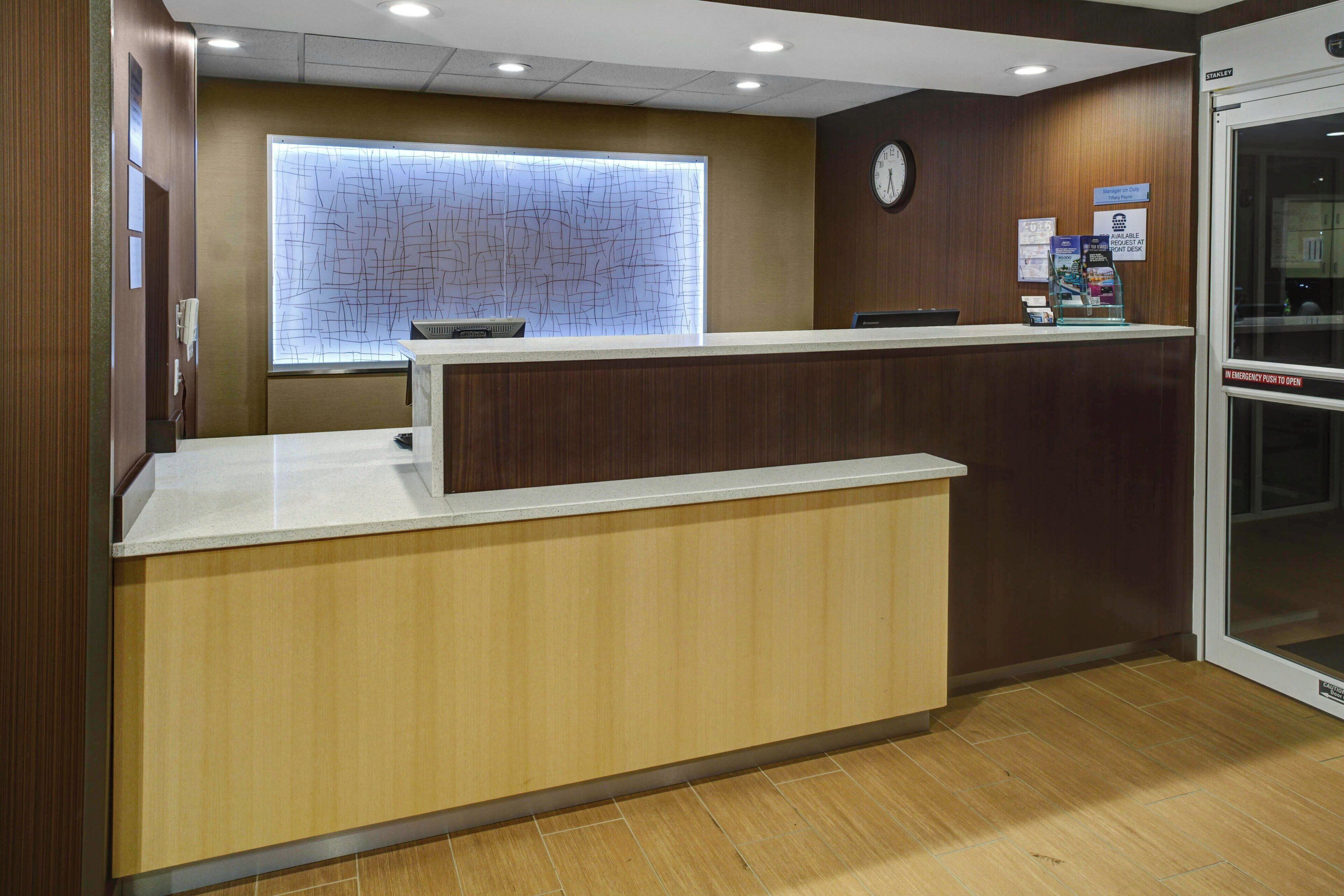 A reception desk with a wooden finish, a clock on the wall, and a window with a view of the outside.