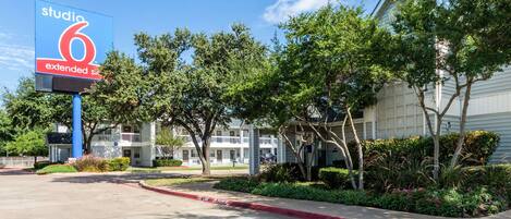 A hotel named 'Studio 6 Extended Stay' with a parking lot, trees, and a building with a white facade.