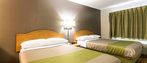 A hotel room with two beds, a nightstand, a lamp, and a window with curtains.