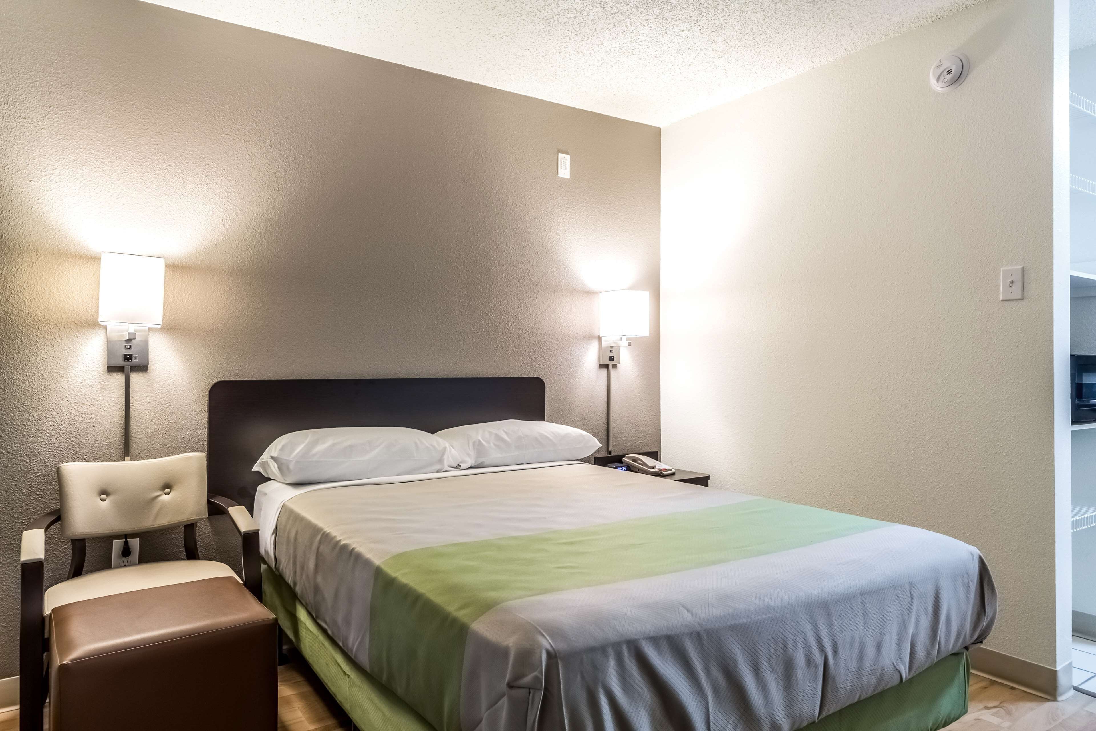 Une chambre d’hôtel comprenant un lit, des tables de chevet, une chaise et deux lampes fixées au mur.