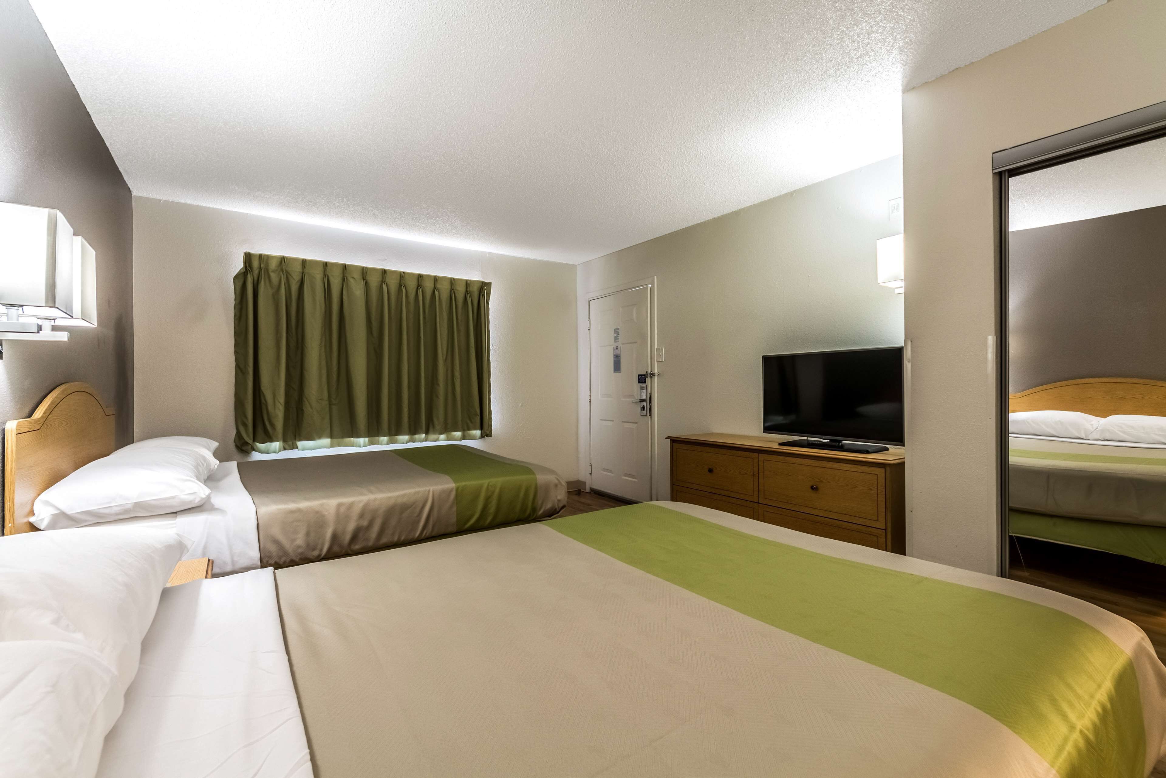 Una habitación de hotel con dos camas, un televisor sobre una cómoda y una ventana con cortinas.
