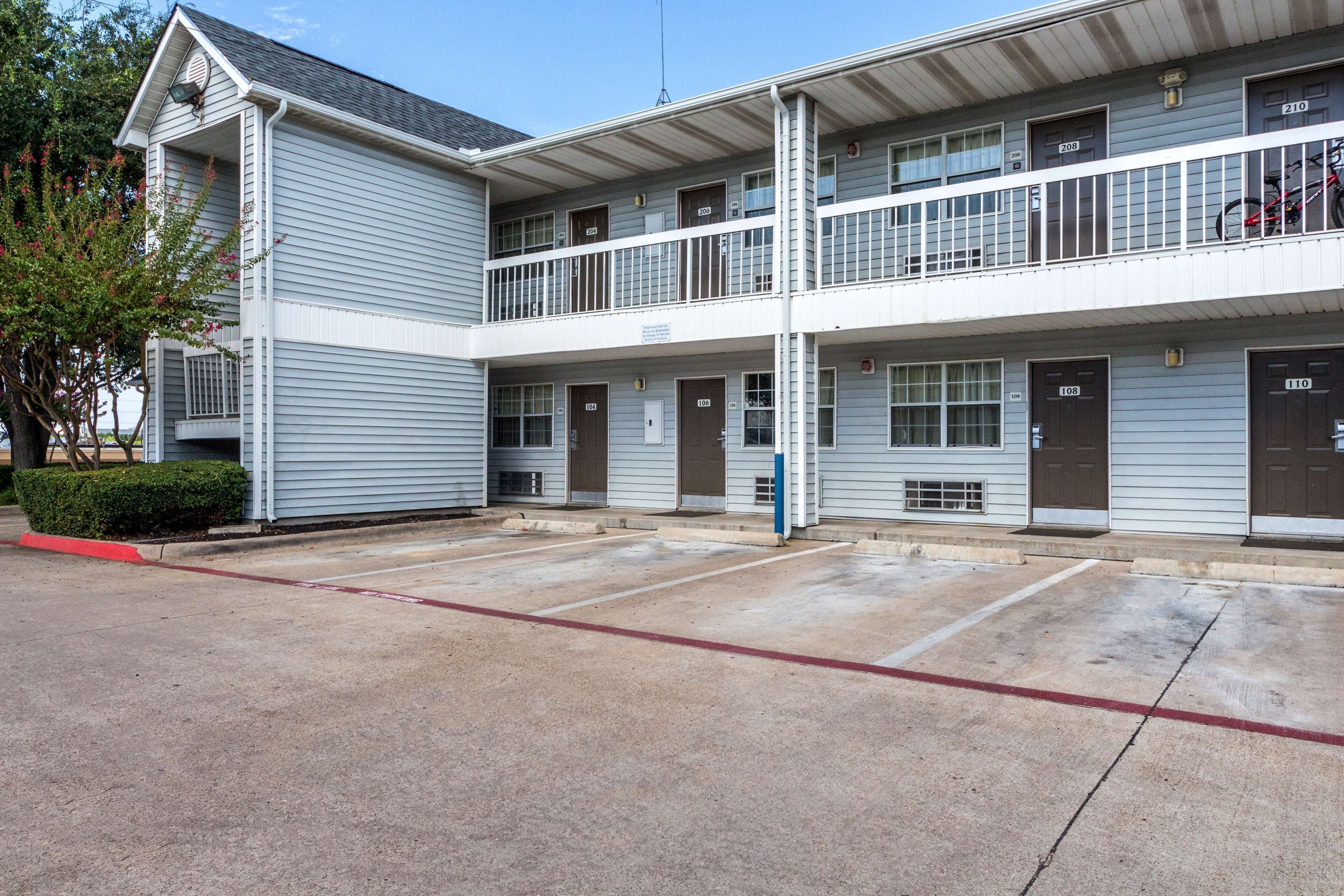A two-story motel with a central courtyard, multiple rooms with doors numbered 108 to 210, and a bike parked on the balcony.