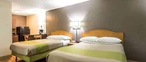 A hotel room with two single beds, a wooden headboard, a desk with a chair, a small table, a lamp, and a television.