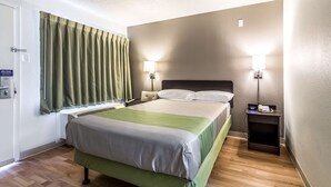 Une chambre d’hôtel avec un lit, une table de chevet, une lampe et une fenêtre avec des rideaux.