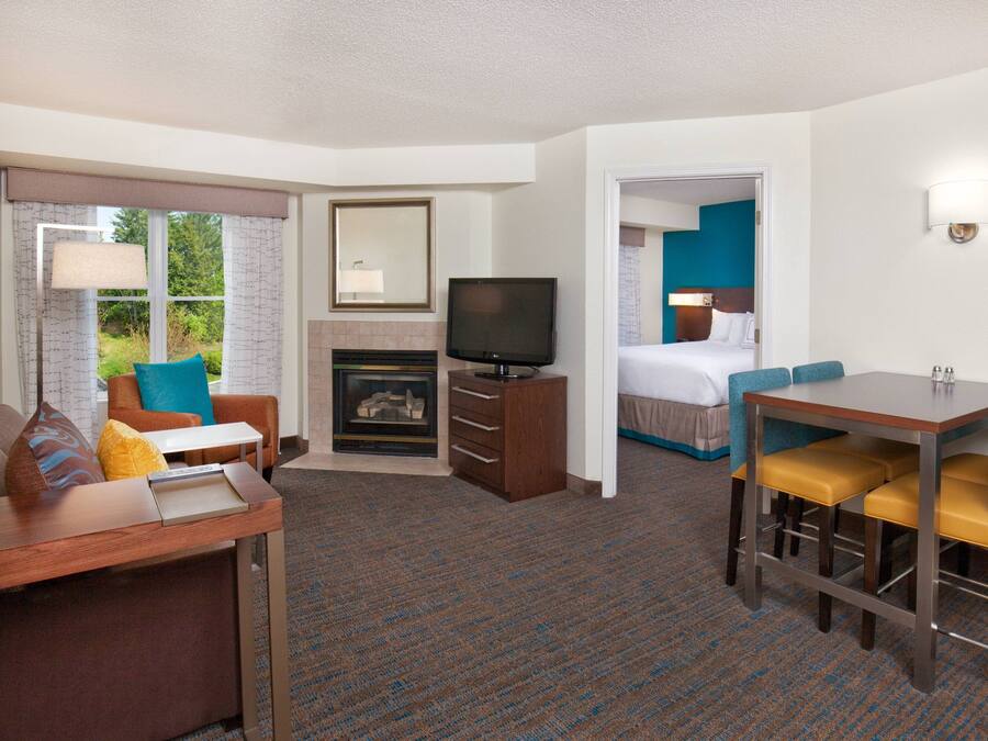 A hotel room with a dining area, a TV, a fireplace, and a bed.