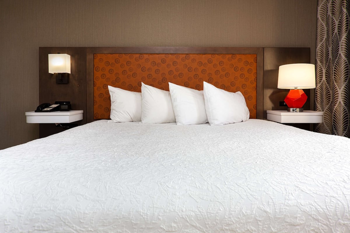 A hotel room with a large bed, a patterned headboard, two bedside tables with lamps, and a telephone on one table.