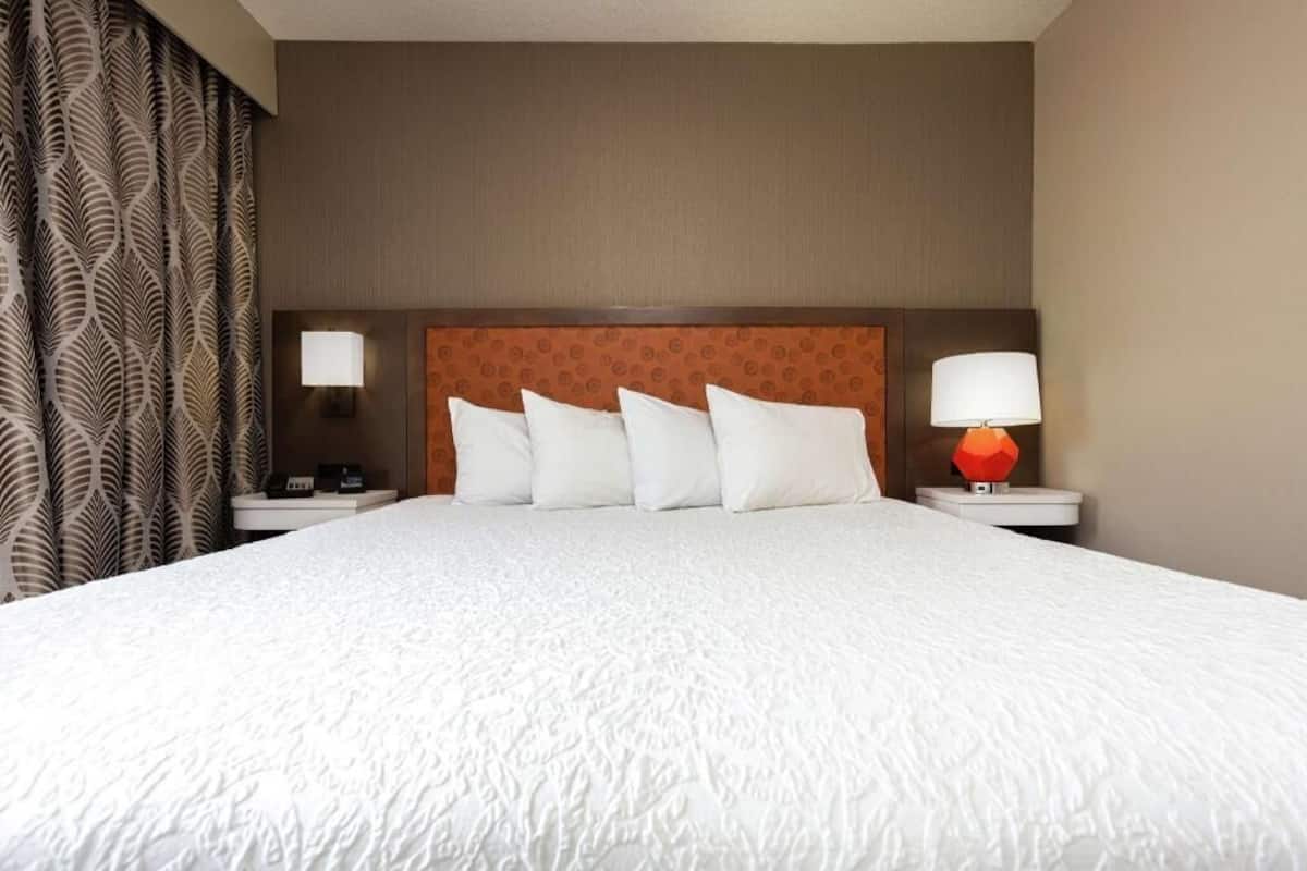 A hotel room with a large bed, two bedside tables, a headboard, and a patterned curtain.
