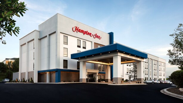 A Hampton Inn hotel with a modern design, featuring a prominent entrance and a gas station canopy.