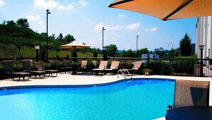 Ein Swimmingpool mit Liegestühlen und Sonnenschirmen, umgeben von einem Zaun und viel Grün.
