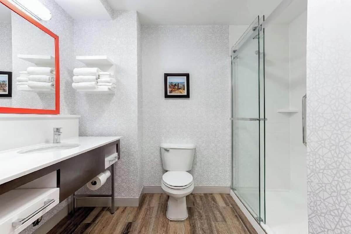 A modern bathroom with a white sink, a toilet, a glass shower enclosure, and a mirror with a red frame.