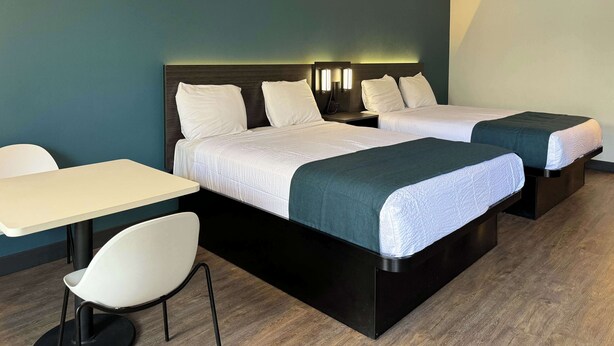 A hotel room with two beds, a desk, and a chair. - Studio 6 Suites Gardena, CA (Gardena)