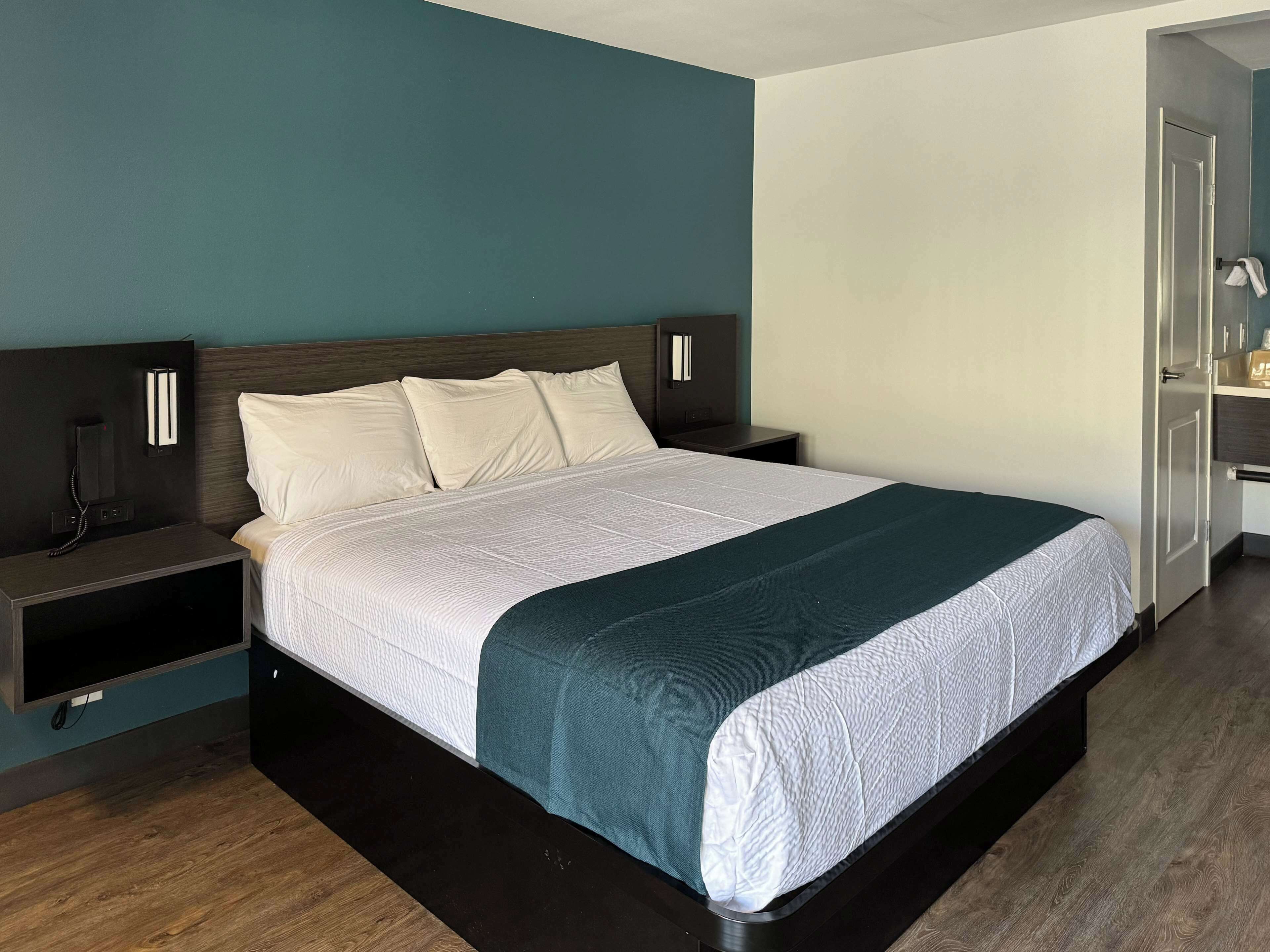 A modern hotel room with a large bed, bedside tables, a desk, and a wardrobe.