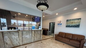 A lobby with a reception desk, a brown leather sofa, a tiled floor, and a ceiling light fixture. - Studio 6 Suites Gardena, CA (Gardena)