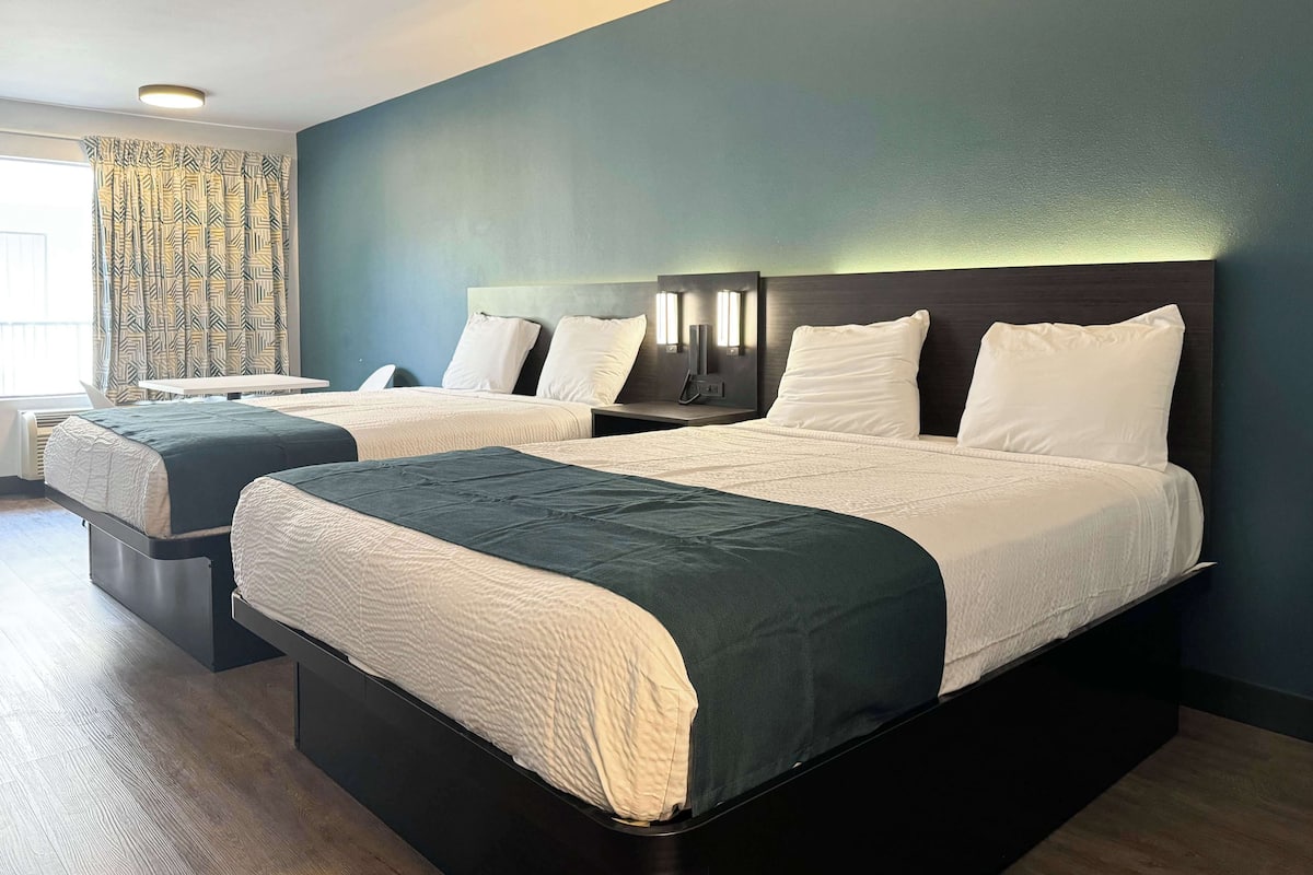 Habitación de hotel con dos camas, un escritorio y una ventana con cortinas.