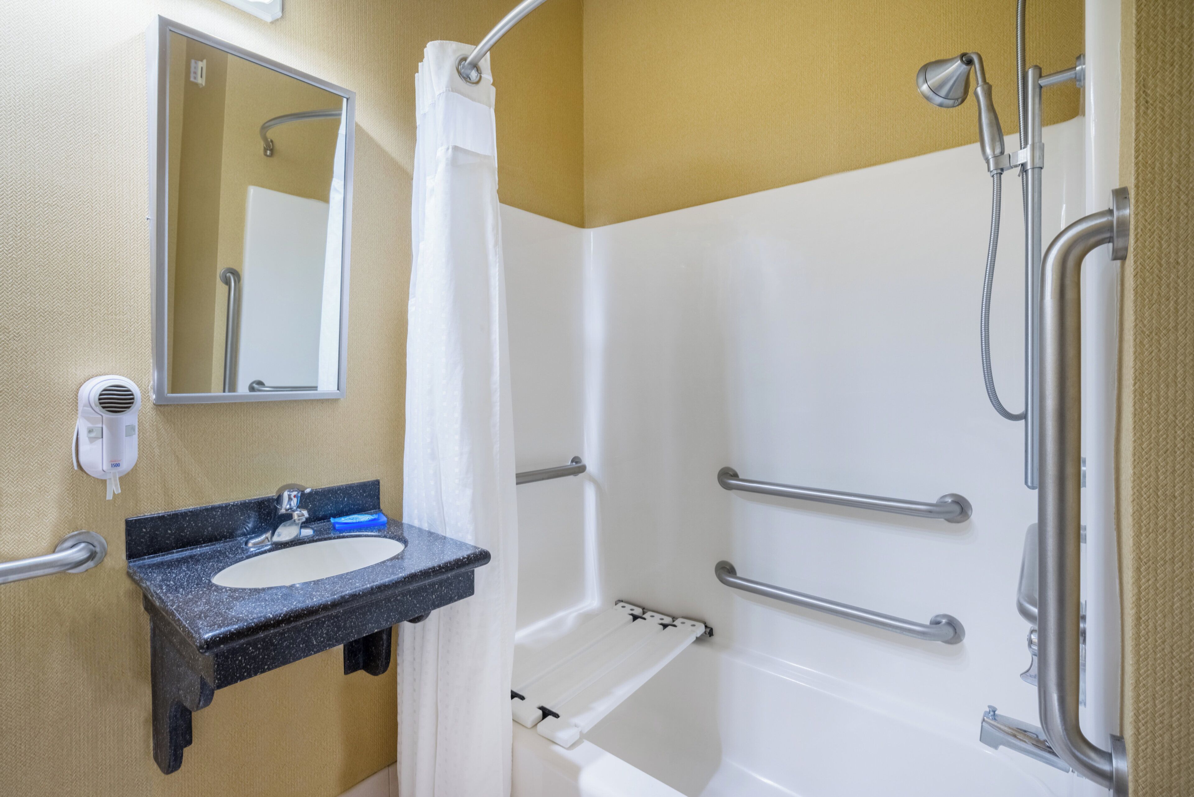 A bathroom with a sink, mirror, shower, and grab bars.
