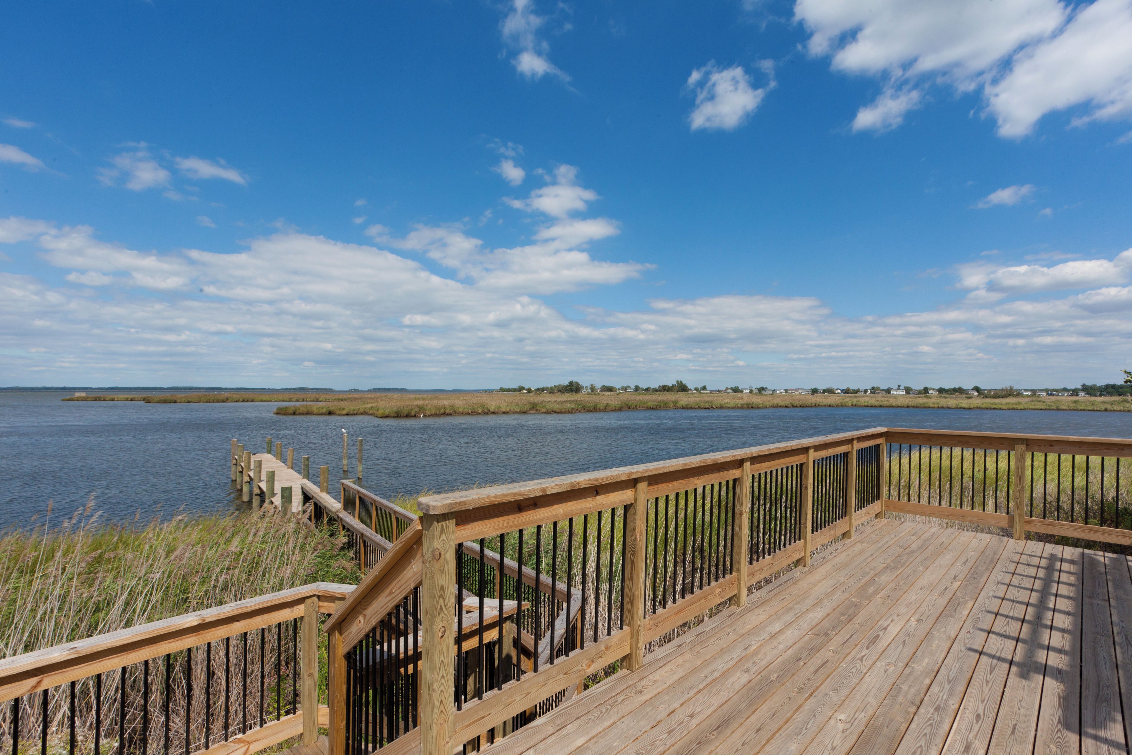 A wooden deck with a railing overlooking a body of water and distant land.
