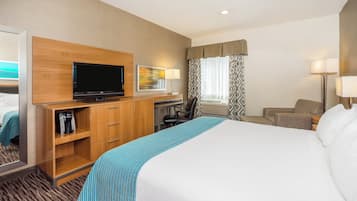 A hotel room with a bed, a desk with a computer, a television, a coffee maker, and a window with curtains.