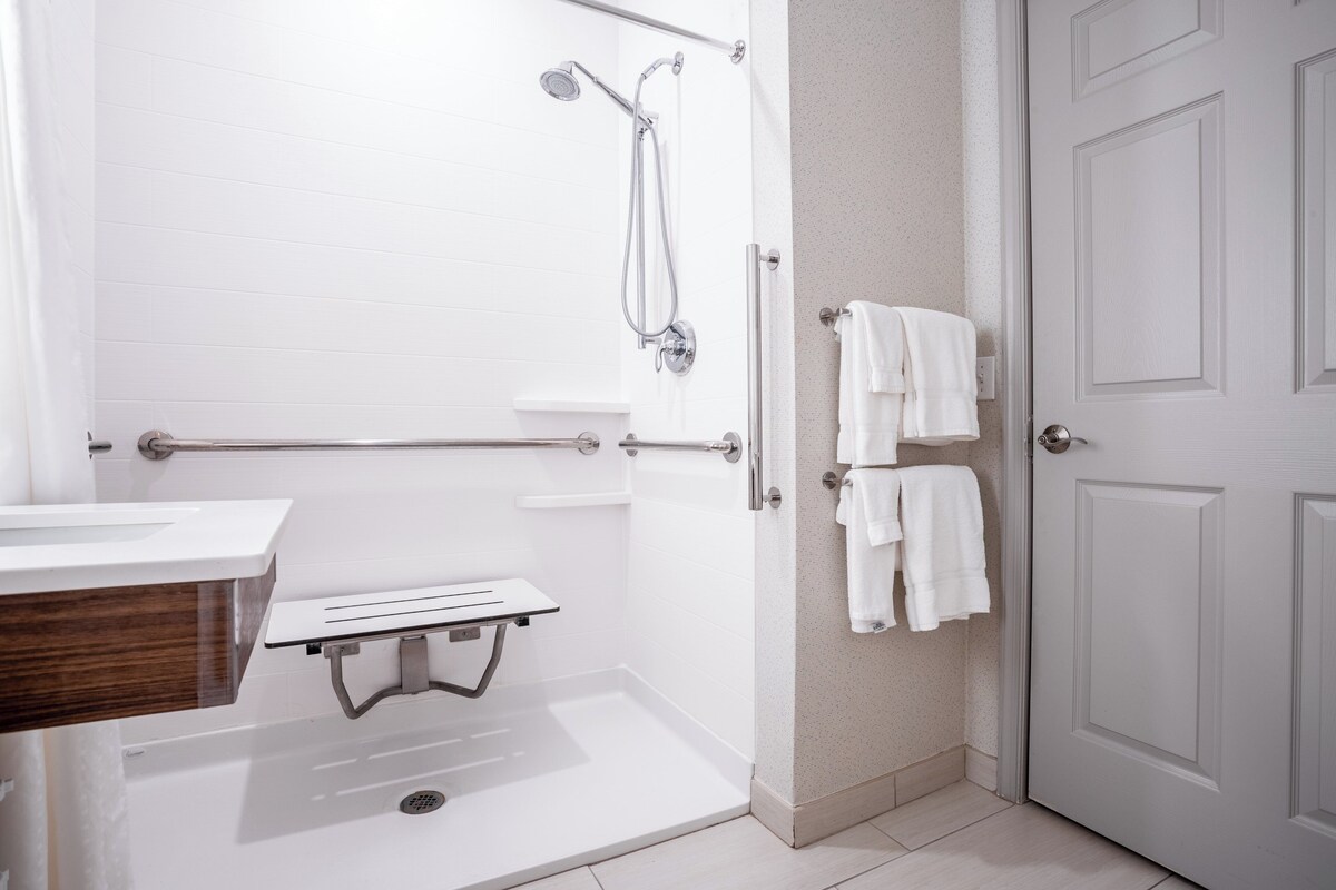 A modern bathroom with a shower, a toilet, and a sink. There are towels hanging on the wall.