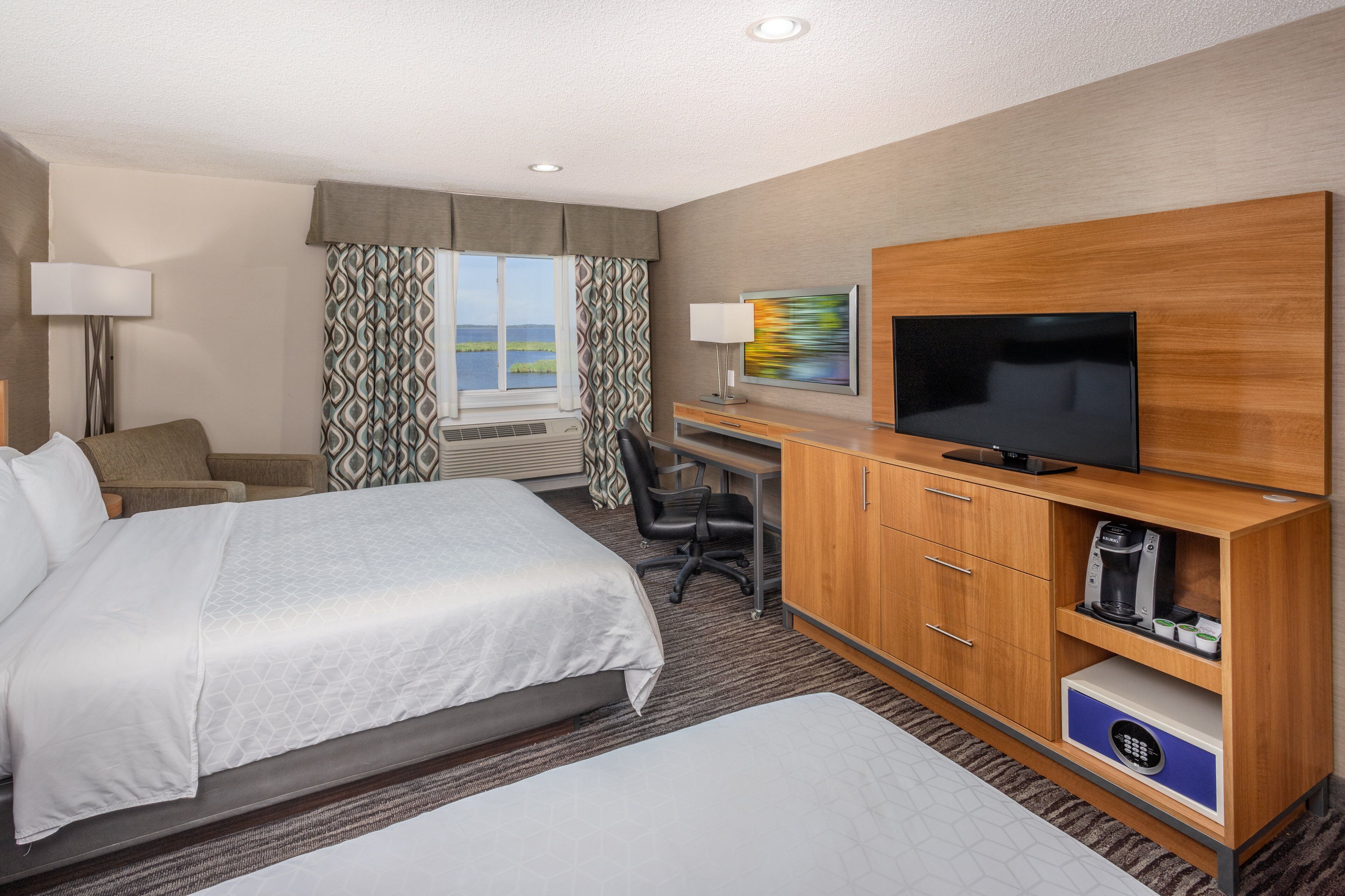 Una habitación de hotel con una cama grande, un escritorio con una silla, un televisor y vistas al exterior.