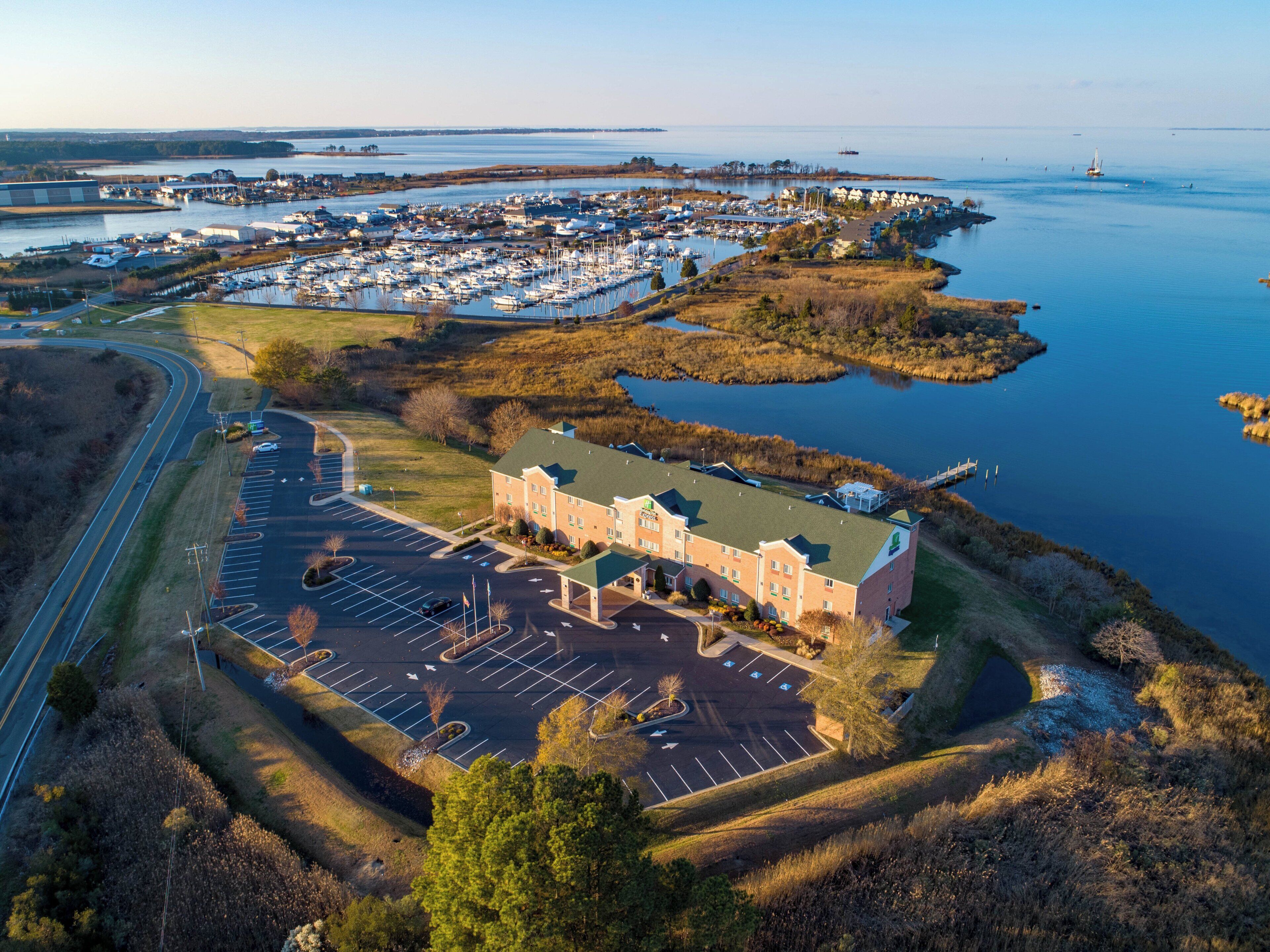 An aerial view of a marina with boats, a parking lot, and a building with a green roof.
