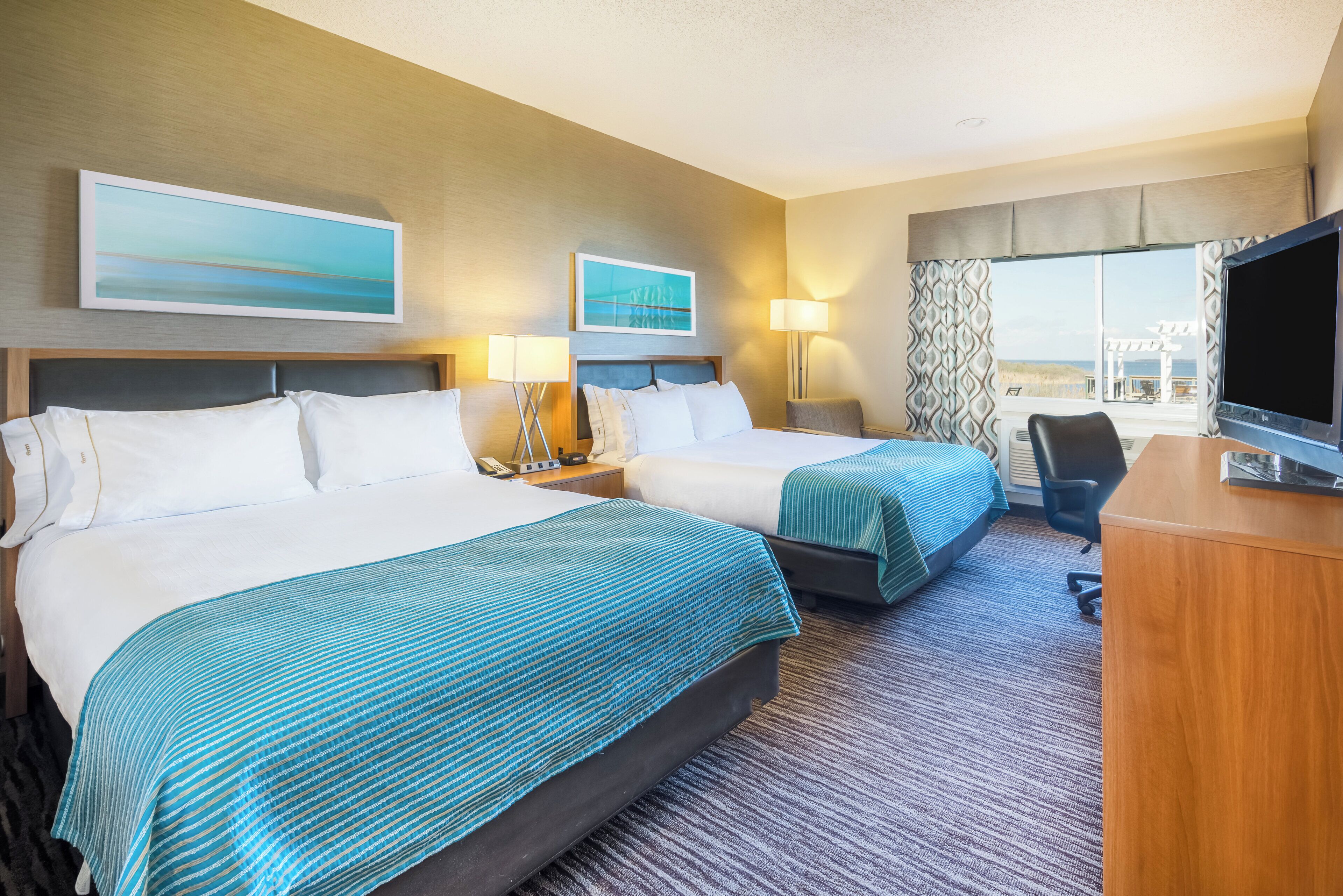 A hotel room with two beds, a desk, a TV, and a window with a view.