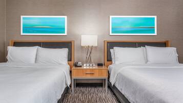 Quarto de hotel com duas camas, uma mesa de cabeceira com abajur e duas fotos emolduradas na parede.