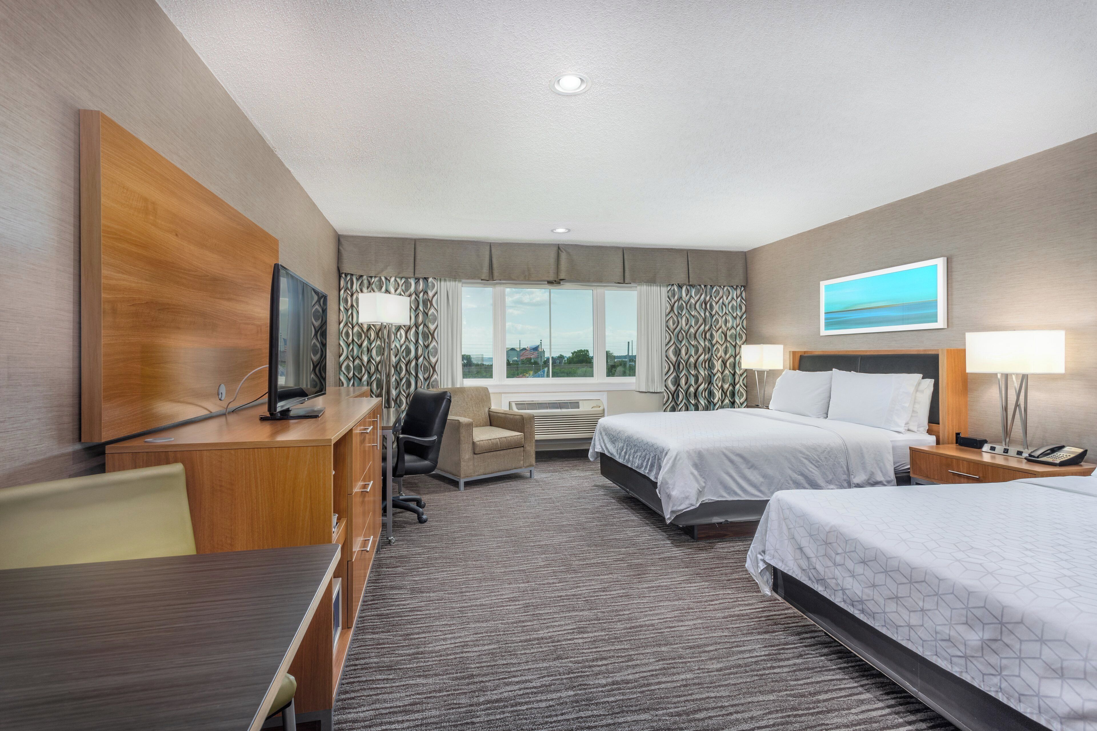 A hotel room with a bed, a desk, a chair, a television, and a window with curtains.
