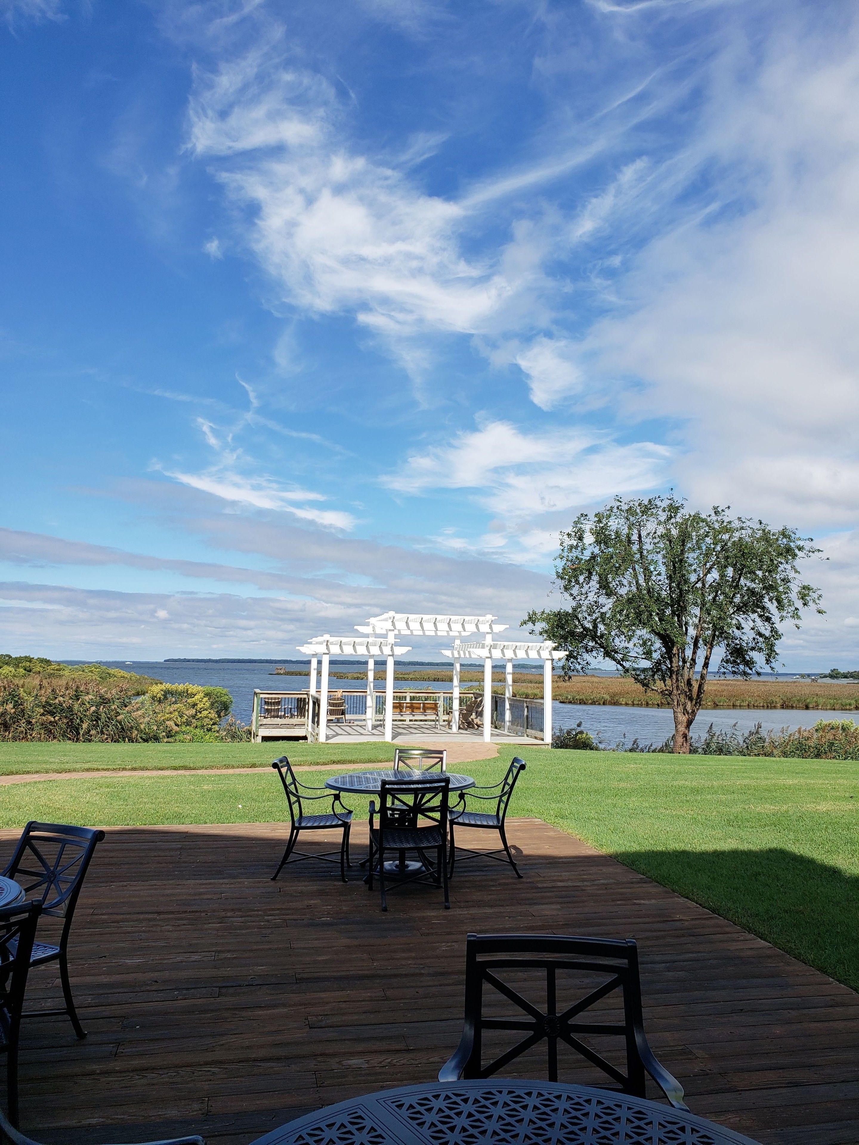 Eine Holzterrasse mit Gartenmöbeln, einer Pergola und Blick auf einen See.