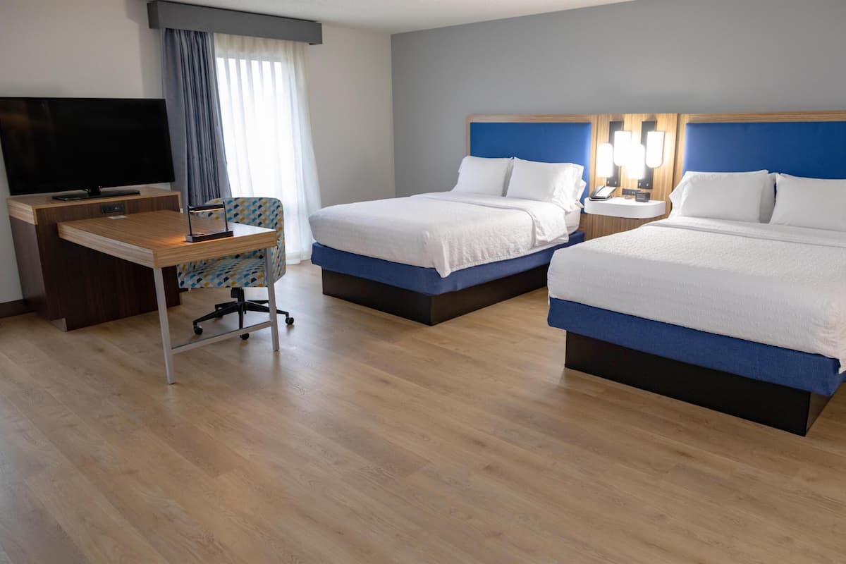 A hotel room with two beds, a desk, a TV, and a window with curtains.