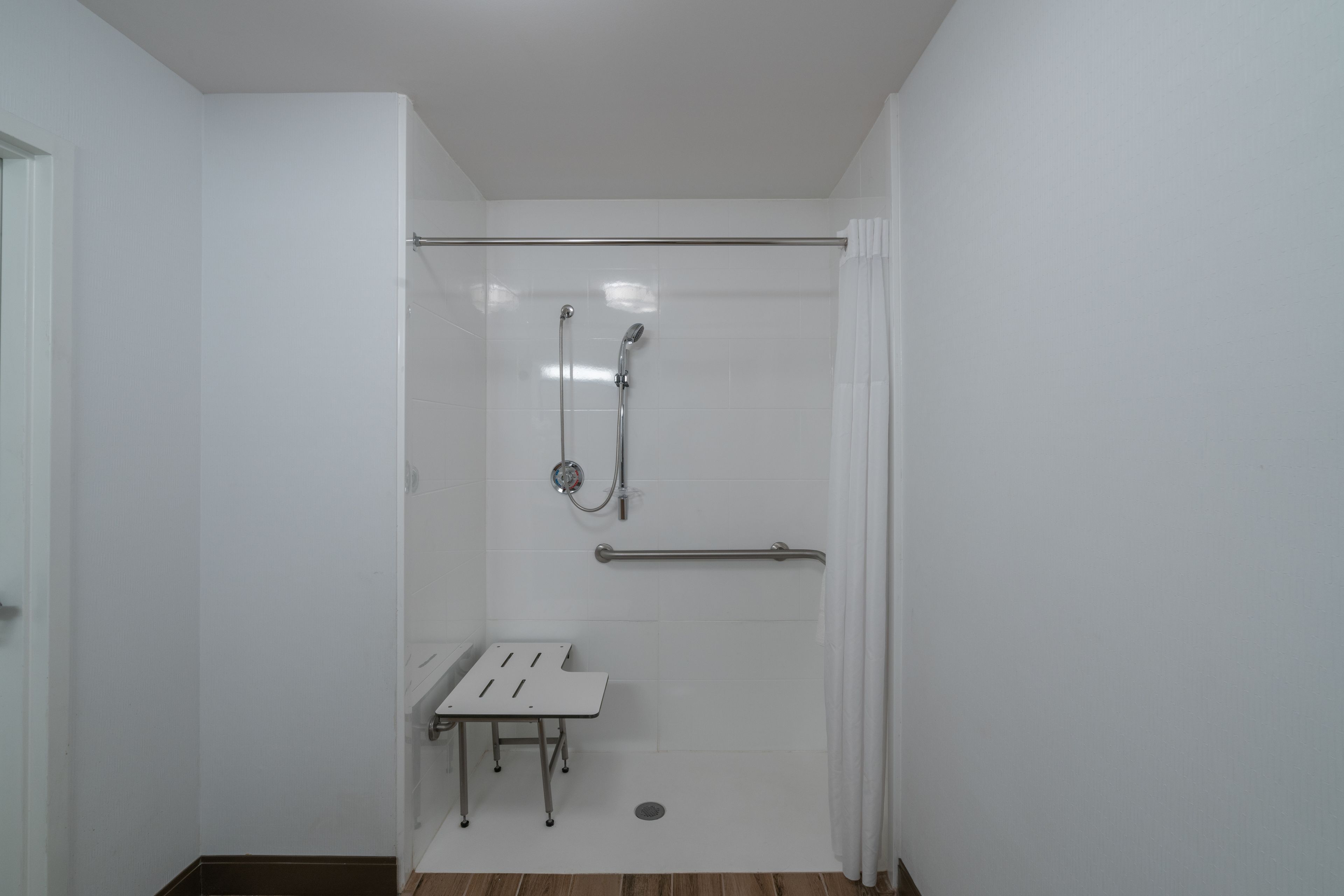 Un baño pequeño y moderno con ducha, barra de apoyo y una mesita.