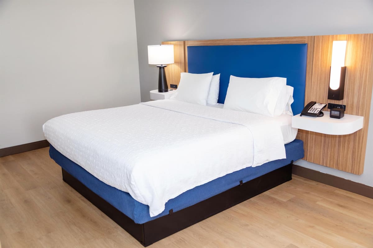 A hotel room with a large bed, a nightstand with a lamp, a phone, and a wall-mounted light.