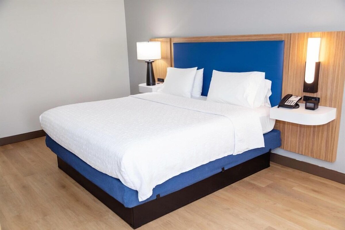 A hotel room with a bed, bedside lamps, a phone, and a wall-mounted light fixture.