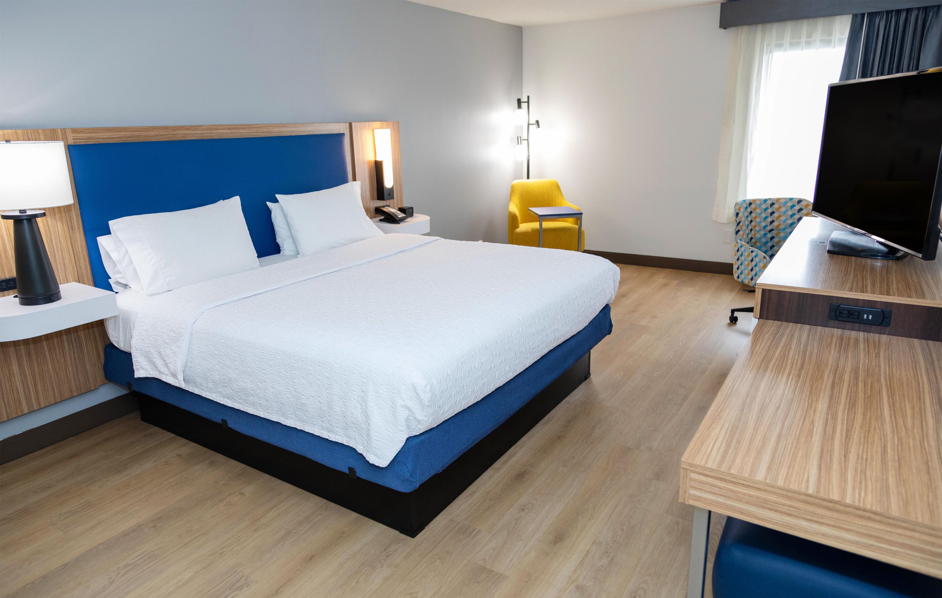 A hotel room with a bed, bedside tables, a desk, a chair, a TV, and a lamp.